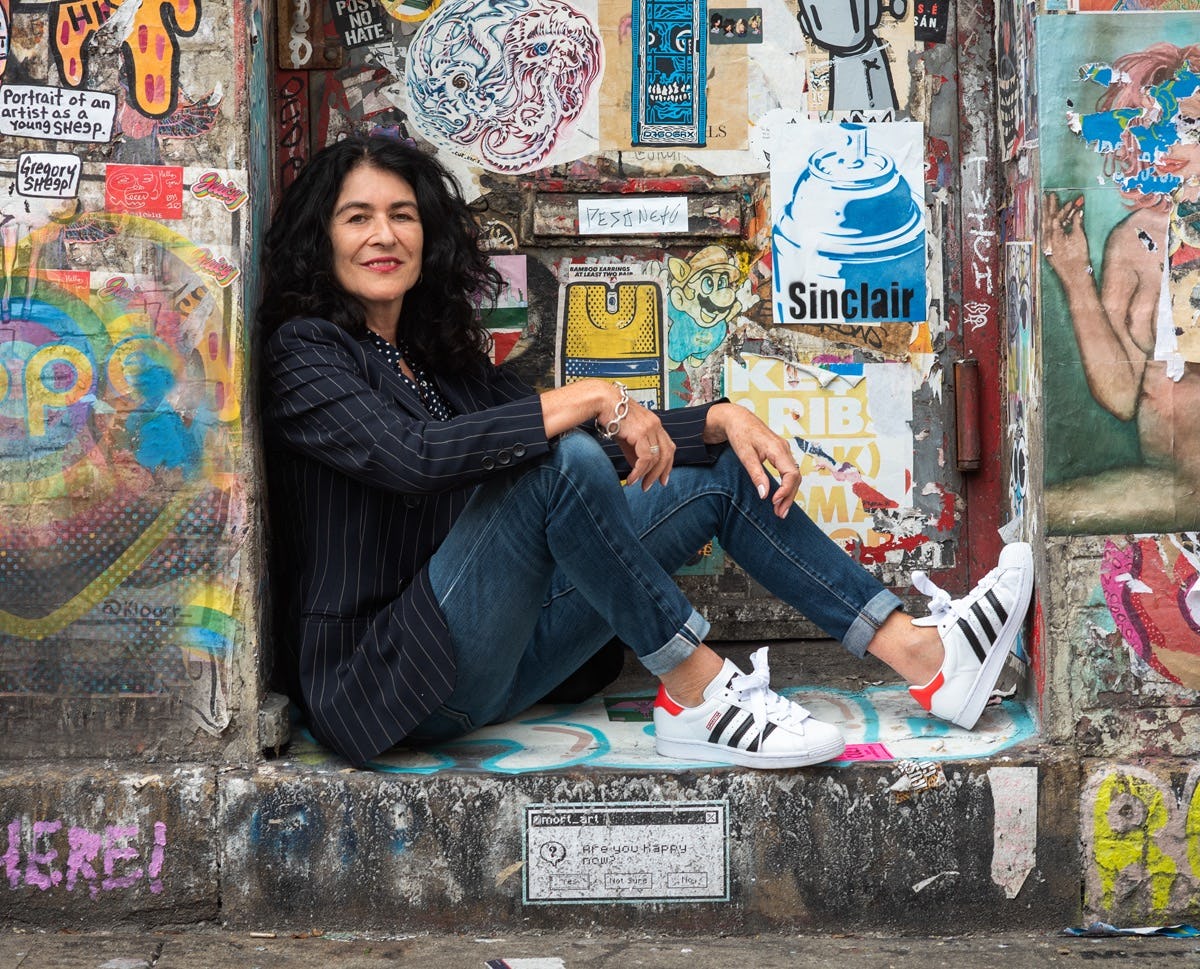 Portrait of the artist Janette Beckman, sitting in front of a graffiti wall. © Gudrun Georges