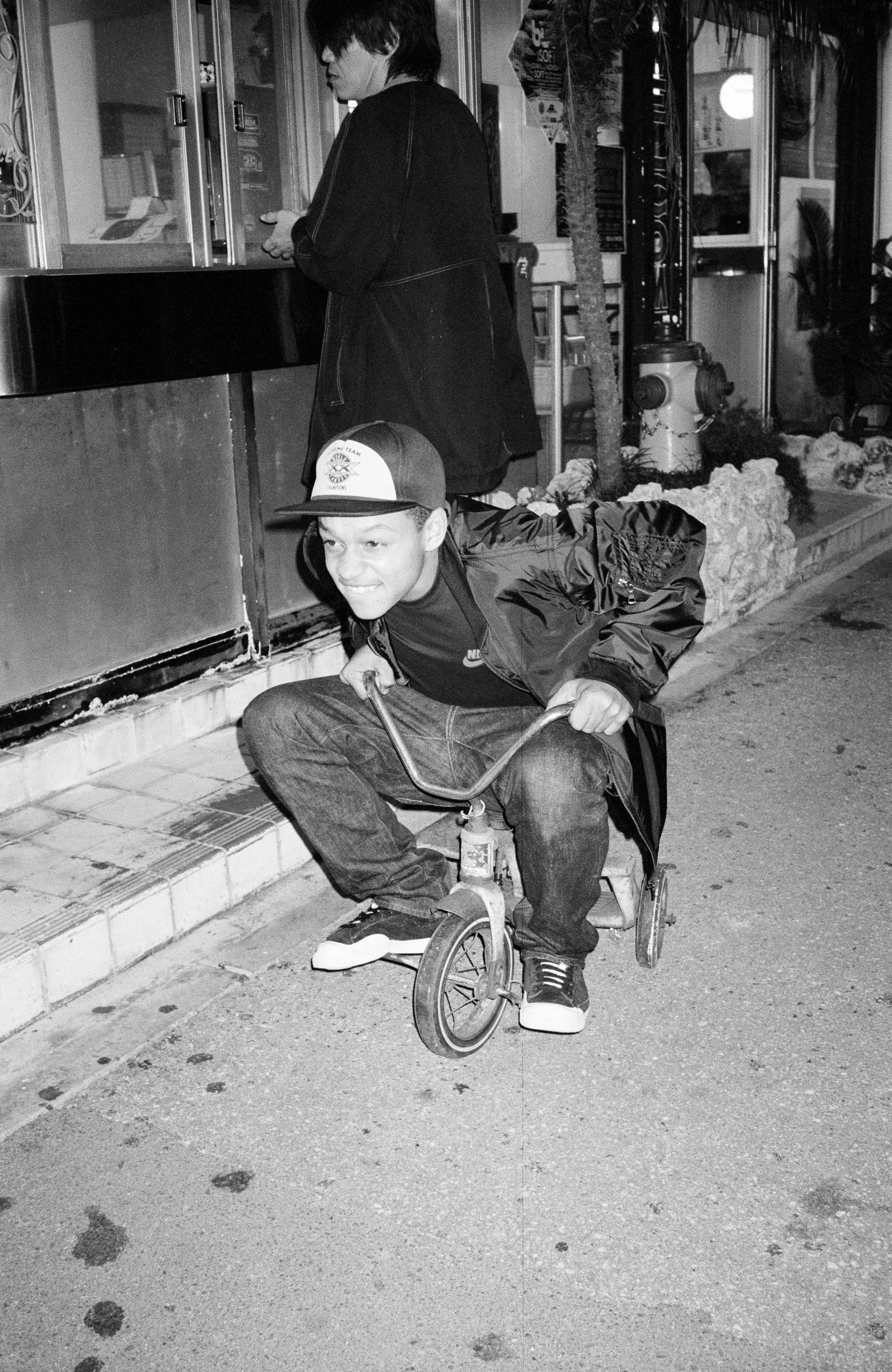 A black and white image of a young man riding a childrens tricycle mimmicking the character Billy from the movie "Saw"