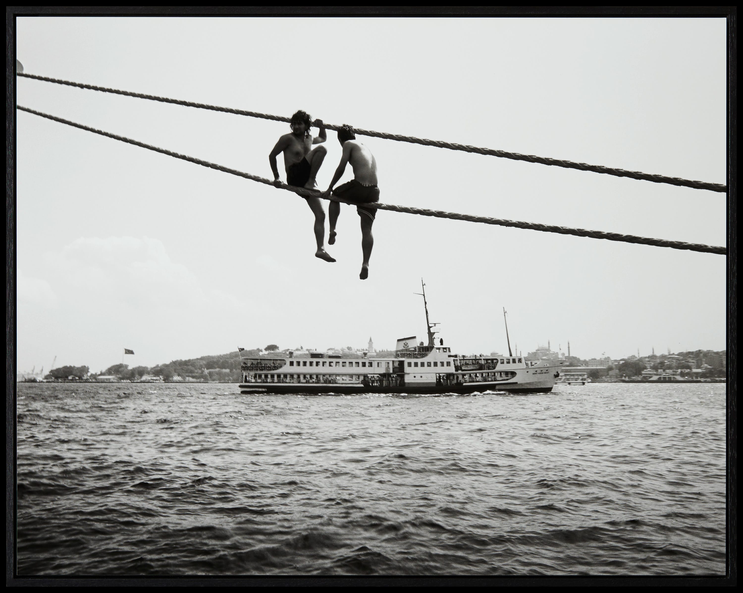 Twee jongens zitten op kabels die over de Bosporus heen gespannen zijn.