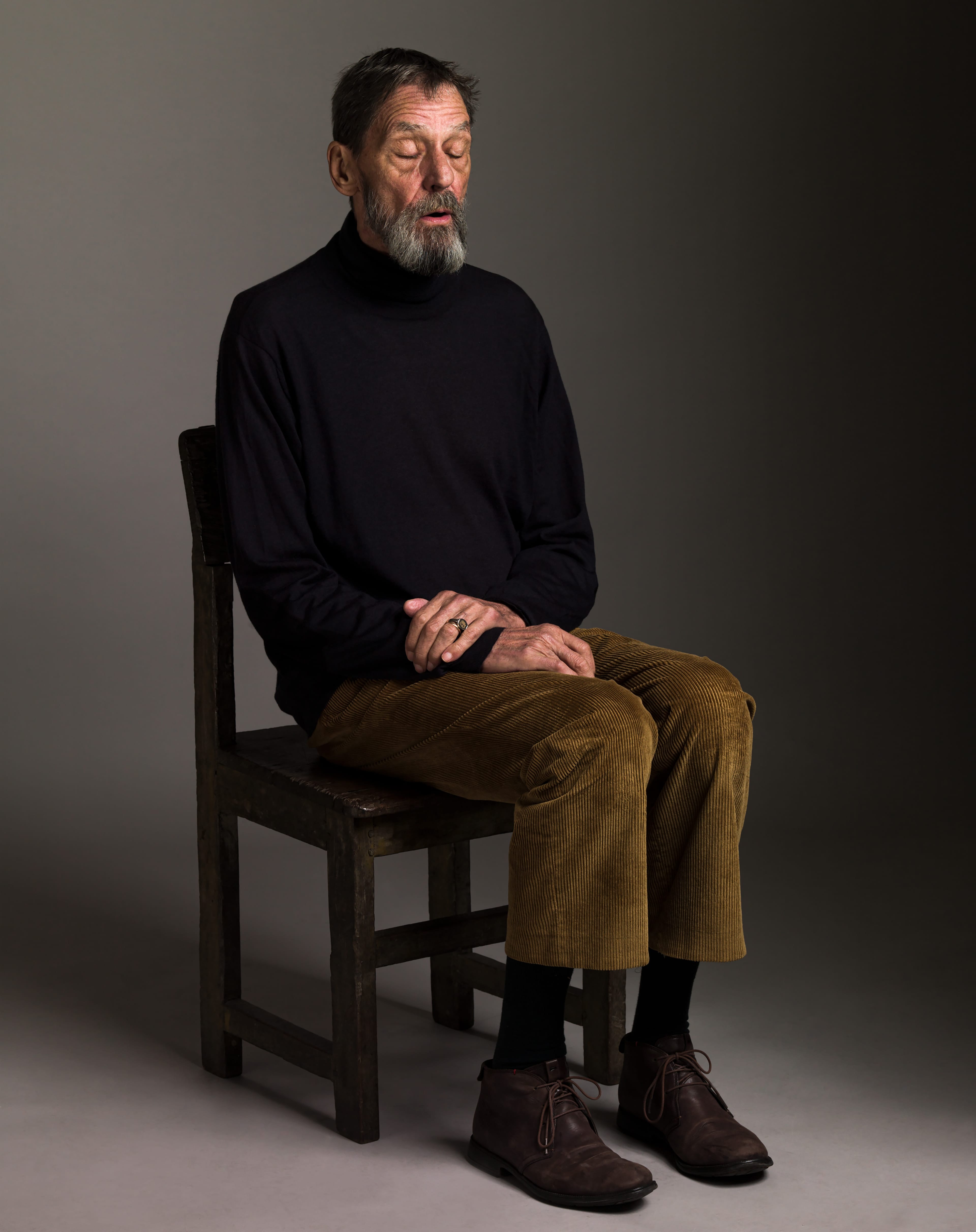 Man with a beard witting on a chair with his eyes closed in a studio.