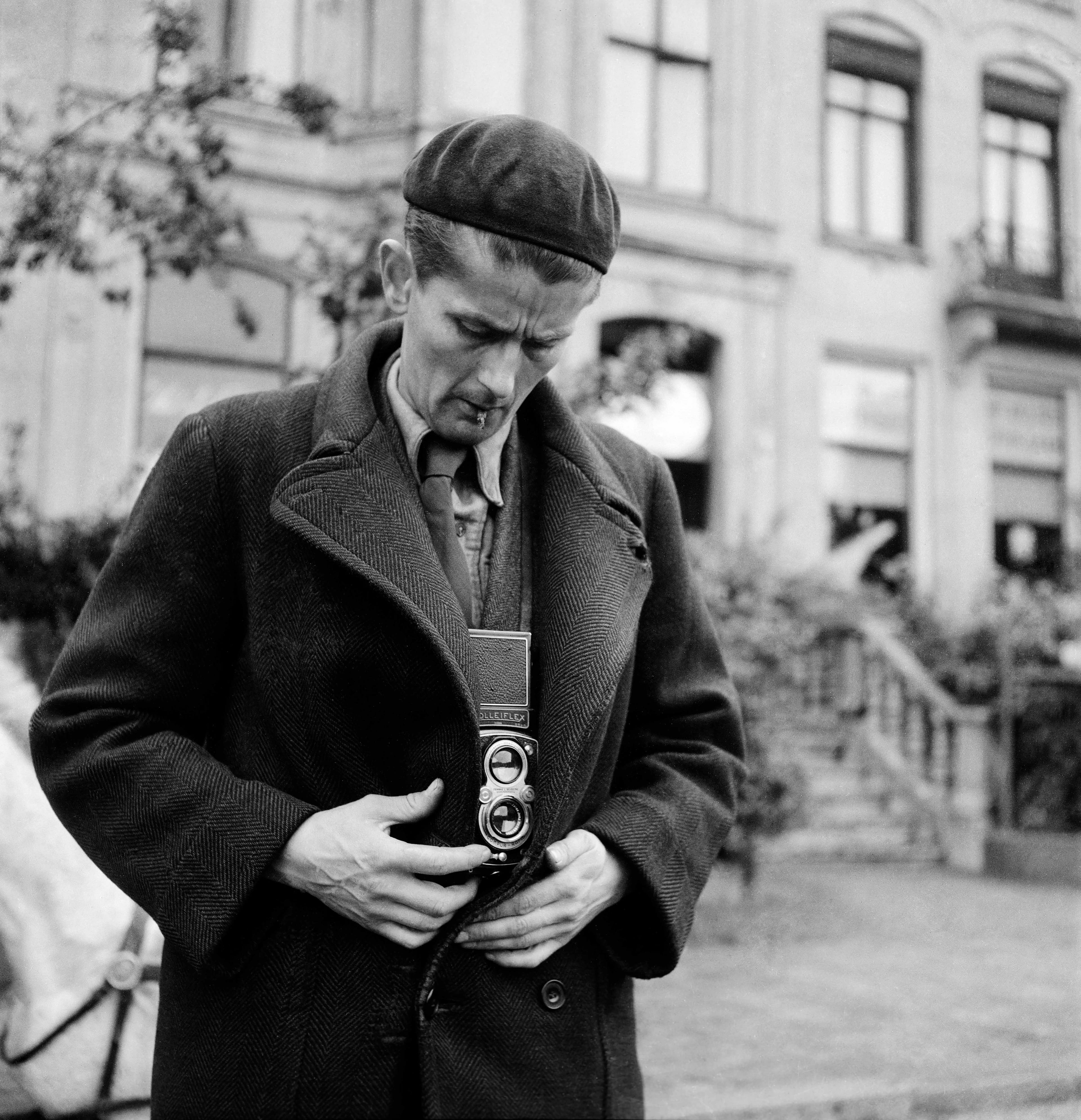 A black and white photo showing a man covering a camera hiddden inside his jacket